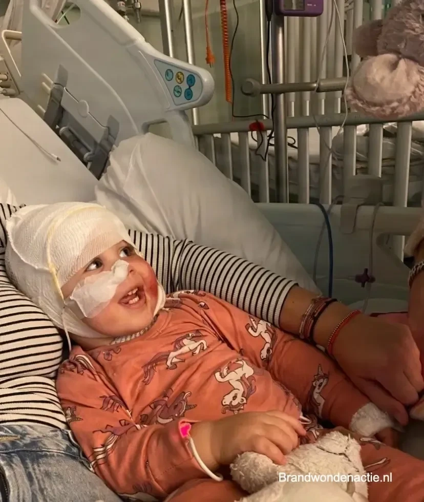 Anne lacht in haar ziekenhuisbed, met een verband om haar hoofd.