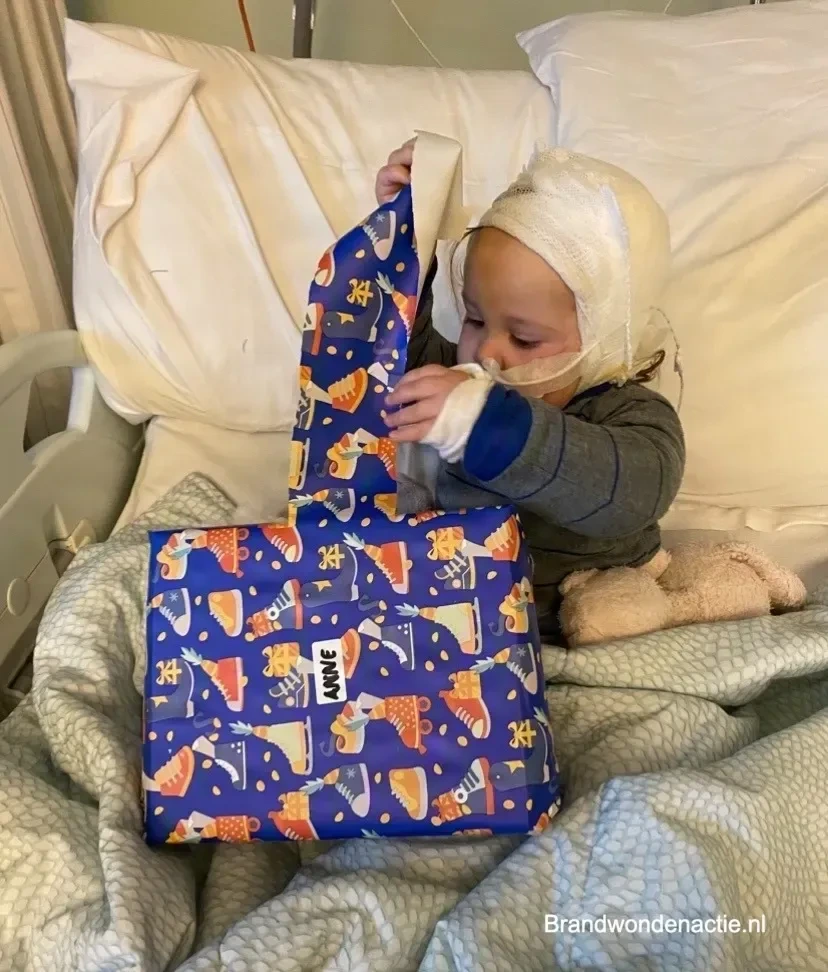 Anne pakt een cadeautje met haar naam erop uit, in haar ziekenhuisbed.